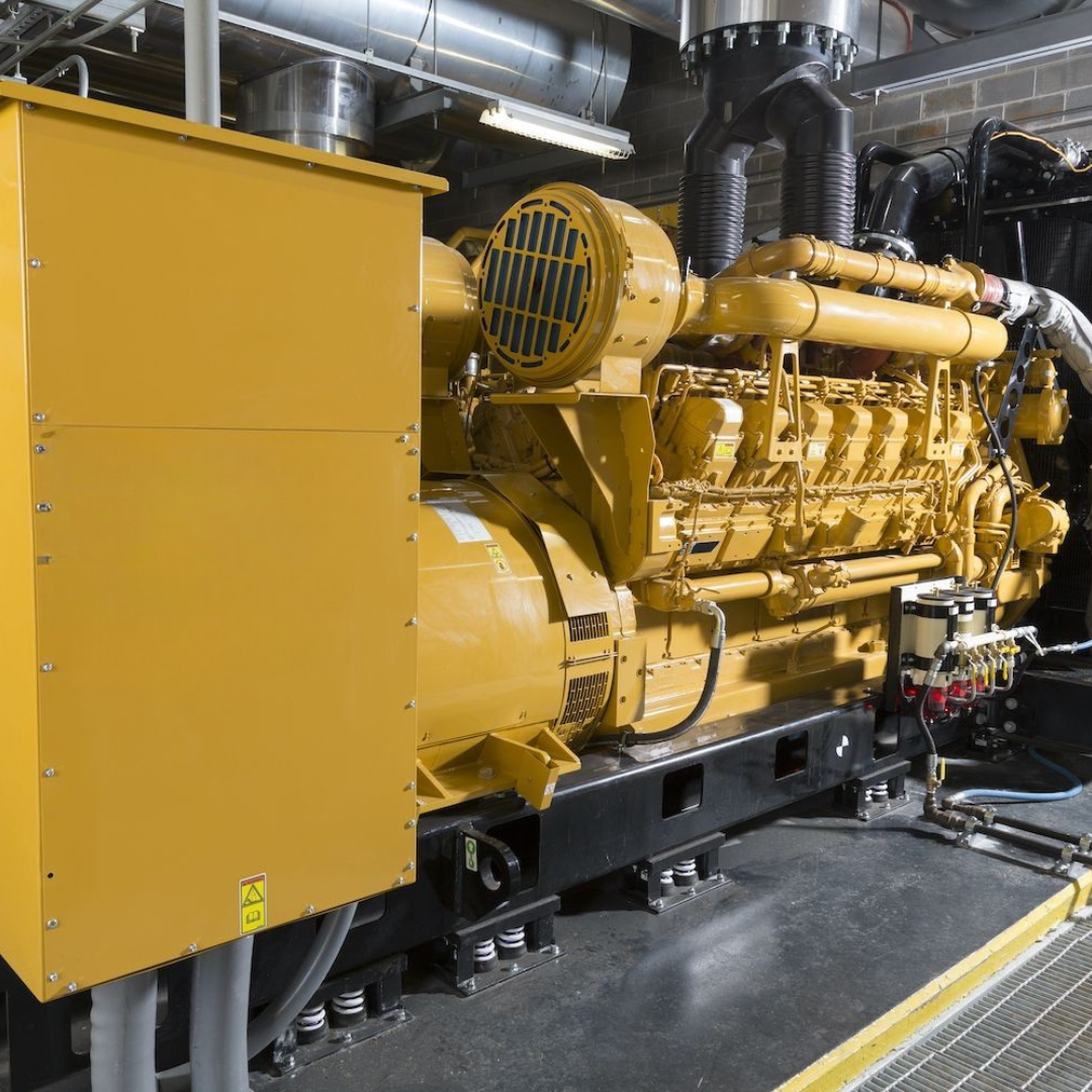 A large yellow emergency generator installed in an industrial setting with pipes in the background.