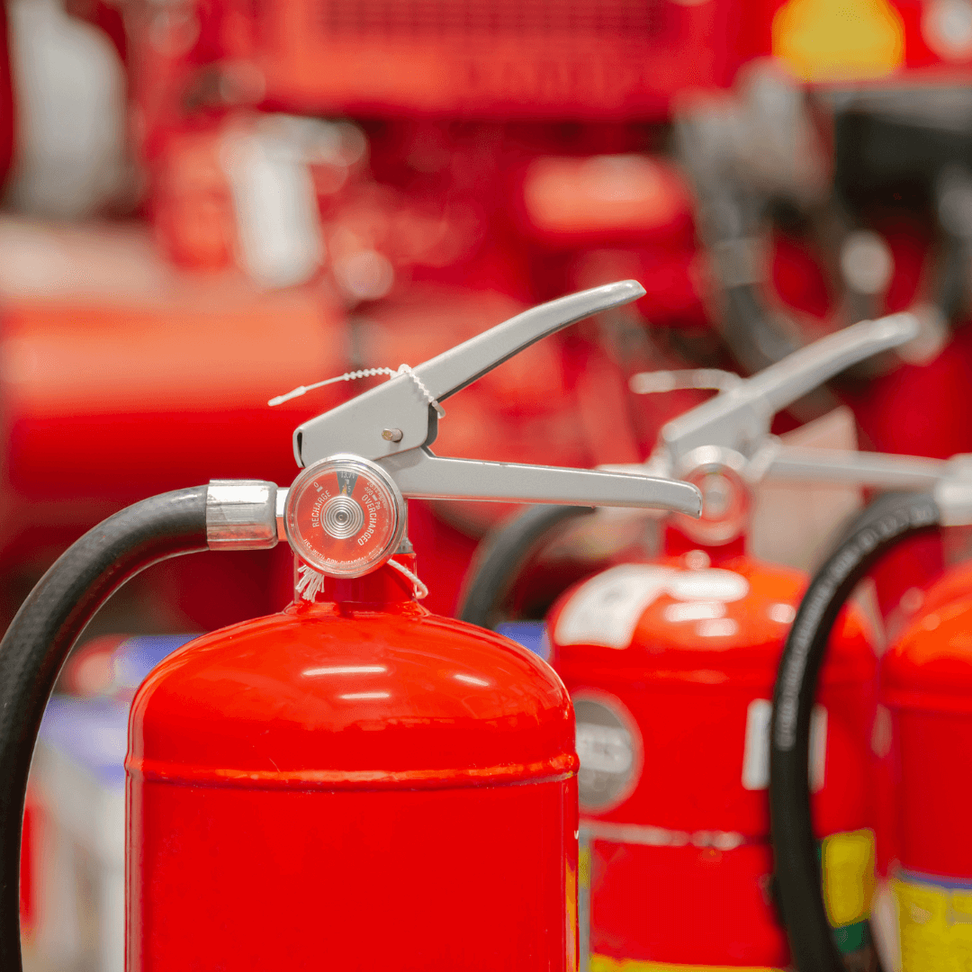 Close-up of red fire extinguishers lined up in a row, showing the pressure gauge and hose.