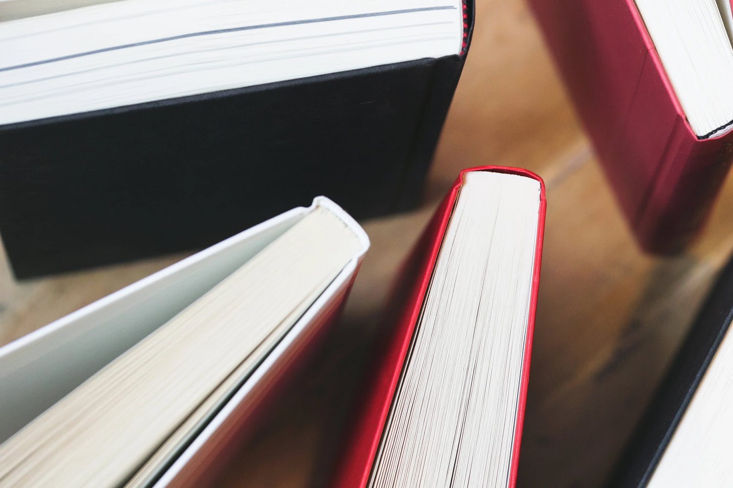 Close-up of the spines and edges of various hard cover books in black and red on a wooden surface.