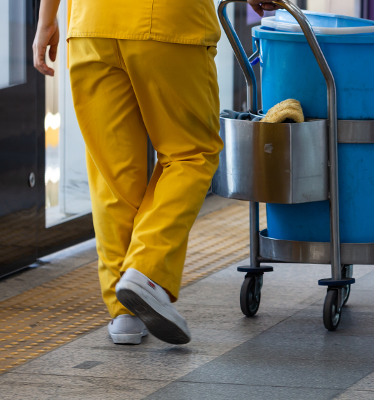 a caretaker in a yellow uniform moving a cleaning cart