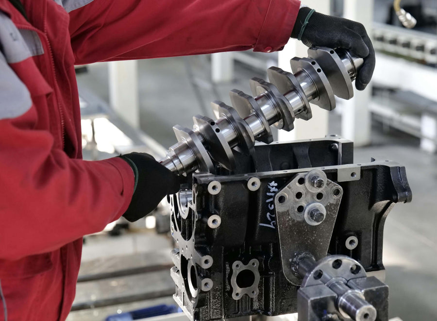 An engineer inserting a large metallic engine piece into an engine block.